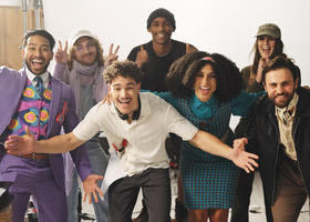 A diverse production crew celebrate the shoot wrap, posing for the camera with celebratory expressions and gestures.