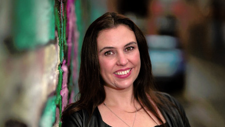 Headshot: Aisling Gallagher, a woman with long, dark hair wearing a black top.