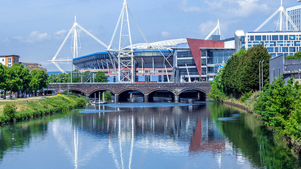 Photograph of a Principality Stadium in Cardiff overlooking the River Taff  a river running through the city next to tall buildings.