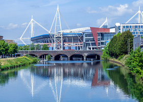 Photograph of a Principality Stadium in Cardiff overlooking the River Taff  a river running through the city next to tall buildings.