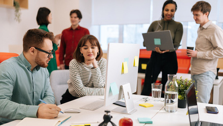 A creative office space with people working at a desk and talking in pairs.