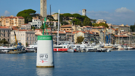 Coastal scene at Cannes with boats docked at the harbour, coloured buildings and blue sky.