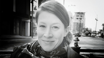 Headshot: Deborah O'Connor, a woman with side part hair tied back wearing a jacket and printed scarf.