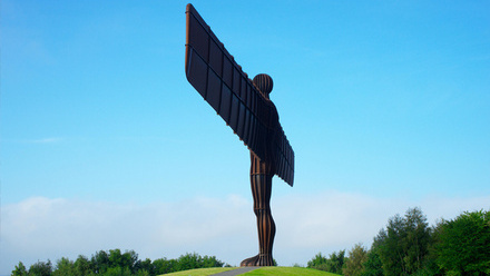 Angel of the North statue in Newcastle Upon Tyne surrounded by blue skies and a green forest.