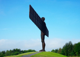 Angel of the North statue in Newcastle Upon Tyne surrounded by blue skies and a green forest.
