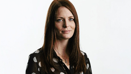 Headshot: Laura Macara, a woman with long, straight brown hair wearing a black and white polka dot shirt. 
