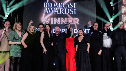 A stage full of people dressed in formal wear, celebrating, with the word 'WINNER' behind them on a large screen.