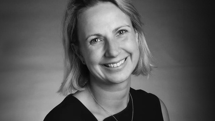 Headshot: Laura Bessell, a woman with bobbed blond hair wearing a black top and silver necklace.