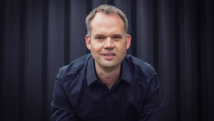 Headshot: Cameron Roach, a man with short brown hair wearing a black shirt.