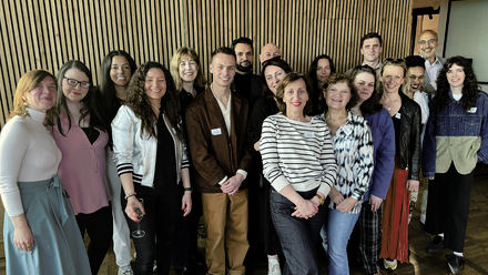 A diverse group of people stand close together, smiling towards the camera.