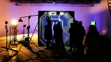 Silhouetted production crew on set in a studio with ambient purple lighting and film equipment. 