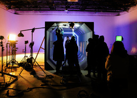 Silhouetted production crew on set in a studio with ambient purple lighting and film equipment. 
