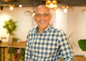 Headshot: Roy Ackerman, a bald man wearing glasses and a checked shirt. 