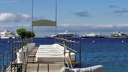 Photo of the Cannes horizon, looking out to sea where four large yachts can be seen. In the foreground are a number of luxury loungers on a jetty.