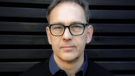 Headshot: Nigel Warner, a man with short brown hair wearing dark-framed glasses and a navy shirt.