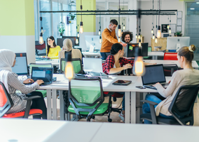 Photo image of an open plan office with colourful chairs and a diverse group of employees spread across the desks.