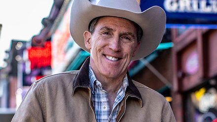 Rob Brydon, a man smiling at the camera wearing a cowboy hat and shirt.