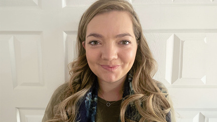 Headshot: Megan Douglas, a woman with long blonde curly hair wearing a brown top and blue scarf.
