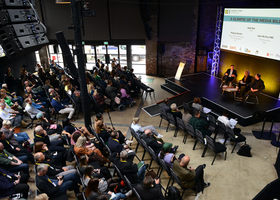Overhead shot of a conference audience facing a stage on the right of the image.