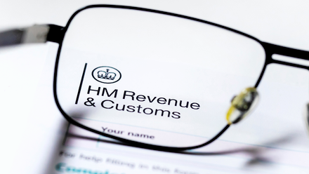 The top corner of a letter clearly marked with the HM Revenue & Customs logo, seen through the lens of a pair of glasses.