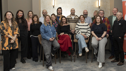 A posed group photo of Pact Future Wales participants with a red Pact banner beside them.