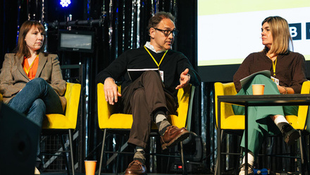 Pact CEO, Nigel Warner on stage speaking in front of a screen, with two other panelists either side of him.
