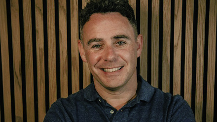 Headshot: Kieran Doherty, a man with short, brown hair wearing a navy blue shirt.