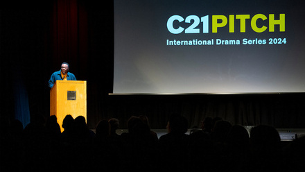 Person pitching on stage in front of a screen reading 'C21 Pitch.'