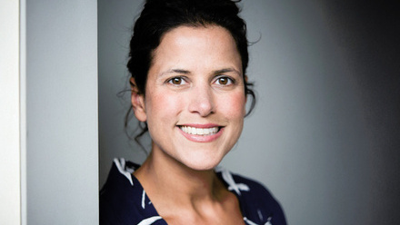 Headshot: Asha Amster, a woman with dark brown hair wearing a patterned, black and white top.