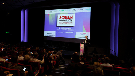Screen Summit presentation on a stage with an audience in a cinema setting.