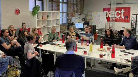 Photo of a group of Pact members and senior staff members sat around a meeting table in the Pact Leeds Office, in discussion.