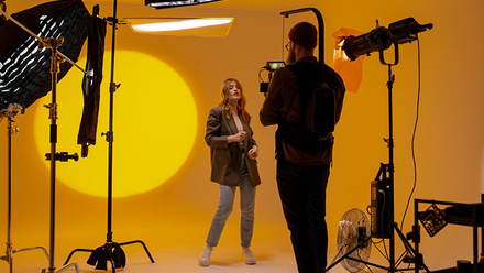 Videographer capturing footage of an actor in a studio with yellow lighting and equipment.
