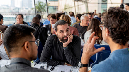 Three people sat having a meeting at a bustling social event with a cityscape view in the background.