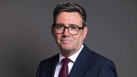 Headshot of Andy Burnham, a man with short dark hair wearing dark-rimmed glasses and a dark blue suit jacket with white shirt and dark red tie.