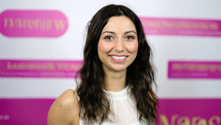 Headshot: Emma Butt, a young woman with long, dark, wavy hair wearing a white top.