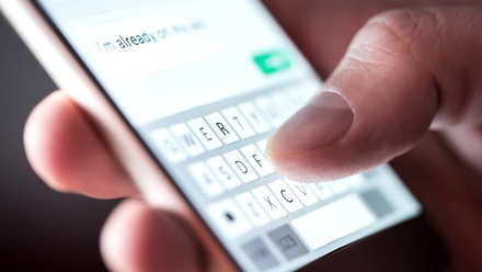 Close up on a hand on a phone screen, typing into a messaging app.