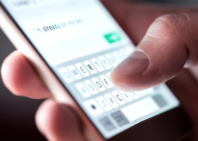 Close up on a hand on a phone screen, typing into a messaging app.