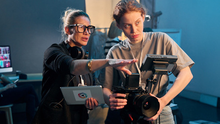 A director wearing headphones and signalling with their hand to a camera operator in a blue room.