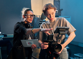 A director wearing headphones and signalling with their hand to a camera operator in a blue room.