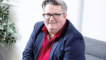Headshot: Chris Curley, a man with white hair, wearing glasses, a blue suit jacket and red shirt.