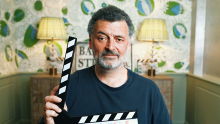 Photo of Stephen Moffat. He is holding a clapper board and looking directly at the camera with one eyebrow raised.
