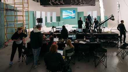 A large film crew sets up in a studio space with camera rigs and lighting equipment.