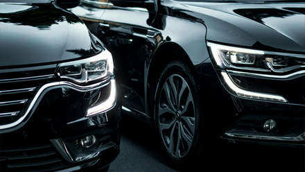 The front end of two shiny, black cars showing the headlights and wheels.