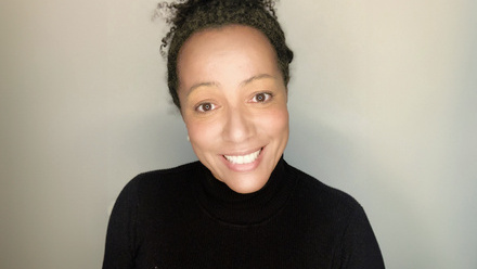 Headshot: Susannah Spring, a woman with dark brown hair tied up in a bun wearing a black polo-neck top.