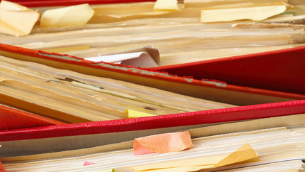 Three red ring binders stacked on top of each other, each full of papers.