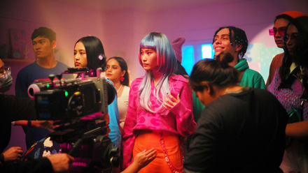 A group of people on a colourful film set, with a camera pointing at them.