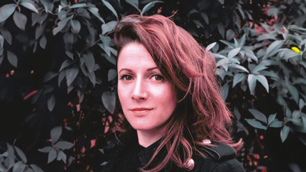 Headshot: Kate Lennon, a woman with auburn hair flicked to the side, wearing a black top.