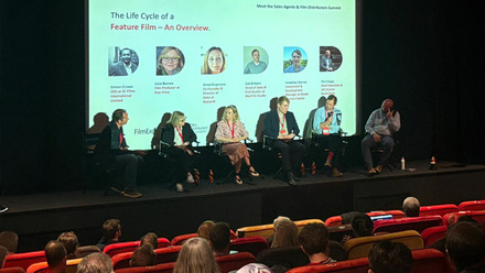 A cinema screening room with a panel of six people sat on stage in front of an audience sat in red cinema seats.