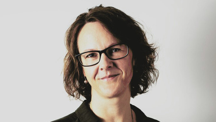 Headshot: Lucy Middelboe, a woman with short, dark-brown hair wearing black glasses and a black shirt. 