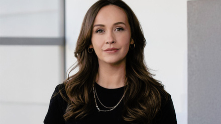 Headshot: Evie Buckley, a young woman with long, brown, curled hair wearing a black t-shirt and silver necklace.